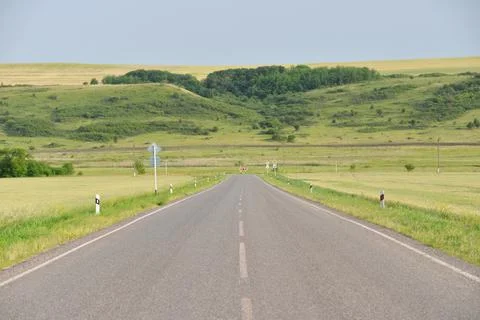 Paved road through green fields and hills in summer Stock Photos