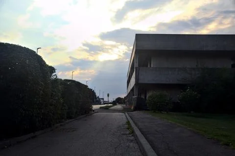 Pavement bordered by a hedge and an abandoned building at sunset Stock Photos