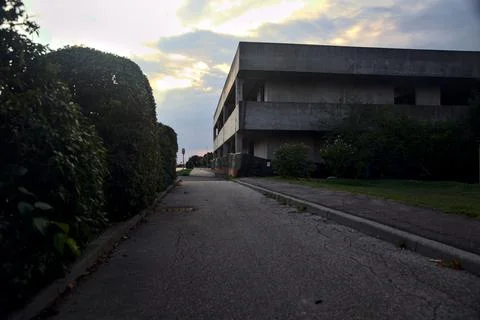 Pavement bordered by a hedge and an abandoned building at sunset Stock Photos