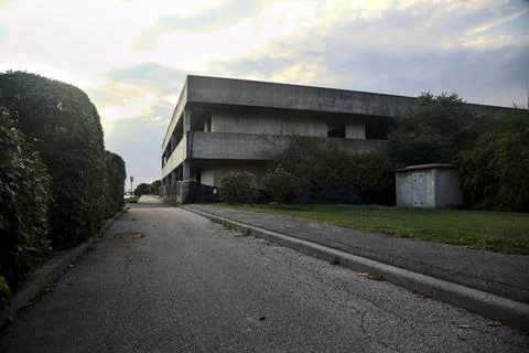 Pavement bordered by a hedge and an abandoned building at sunset Stock Photos