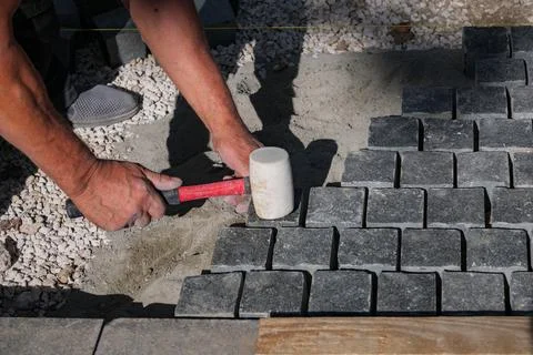 Paver installing granite cobblestone with rubber mallet on sidewalk site Stock Photos