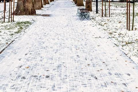 Paving paths in the park, covered with the first snow in winter. Stock Photos