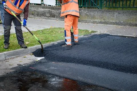 Paving workers adjust new layer of asphalt with shovels in reconstruction of  Foto stock