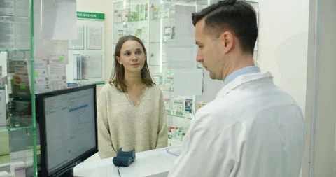 Payment in a pharmacy. Smiling pharmacist proposing woman a payment terminal Stock Footage 167766689