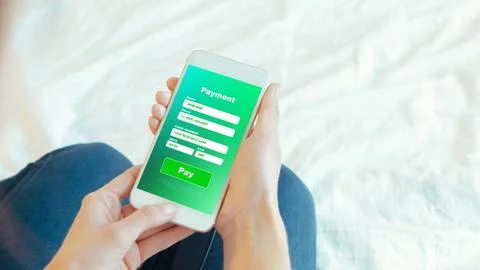 Payment process on a mobile device while sitting on a bed in a home setting Stock Photos