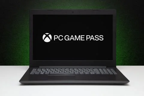PC Game Pass logo on screen laptop computer on black textured wall with green Stock Photos