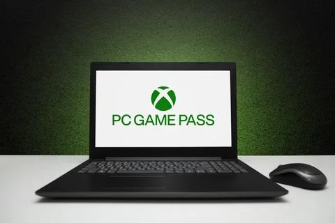 PC Game Pass logo on screen laptop computer with mouse on black textured wall Stock Photos