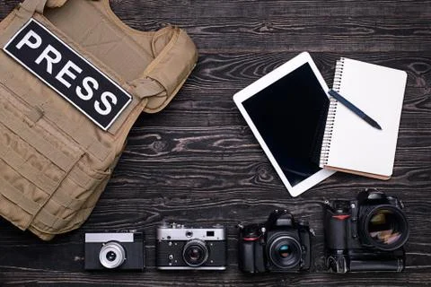 PC tablet and notebook, body armor and photo cameras on wooden table Stock Photos
