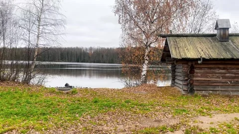 Peaceful autumn scene featuring a rustic wooden cabin by a calm lake, surro.. Stock Footage 319957741