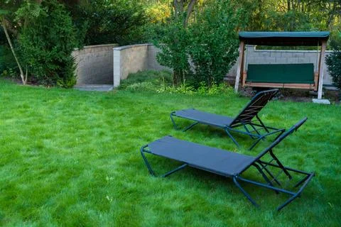 Peaceful backyard featuring two garden loungers and a swing bench set on a lush Stock Photos