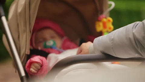 Peaceful infant resting in a stroller while a caregiver gently checks on the 動画素材 336934285
