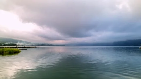 Peaceful Lake View Under Dramatic Cloudy Sky with Mountain Reflections Stock Footage 339417705