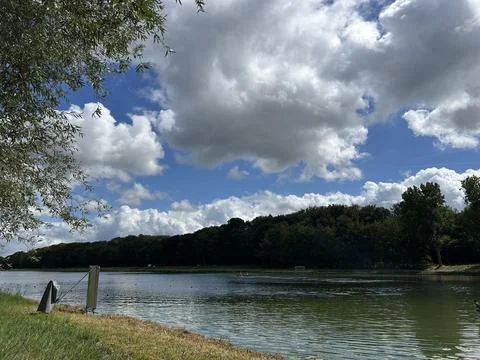 Peaceful lakeside landscape with dramatic summer clouds above calm water, tree Fotos Stock