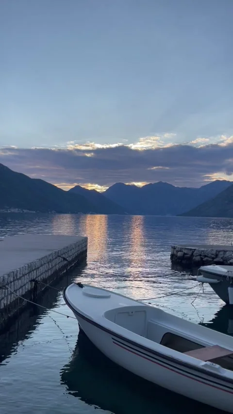 A peaceful lakeside view at sunset, featuring a small white boat moored at a sto Stock Footage 296178486