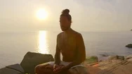 Peaceful Man Meditating On Rocks Near The Seaside During Sunset Stock Footage
