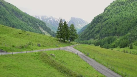 A peaceful mountain road winds through a lush green valley, flanked by trees and Video stock 282735034
