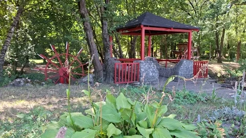 Peaceful Park Gazebo and Rustic Watermill Wheel Surrounded by Greenery Stockbeeldmateriaal 345632213
