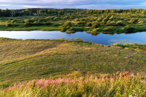 A peaceful river flows gently through vibrant green landscapes Stock Photos