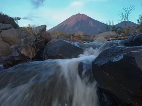 Peaceful river stream flows over rocks beneath Mount Semeru Stock Photos