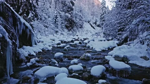 Peaceful slow motion flight over a snow-covered alpine stream with falling snow. Stock Footage 323802731