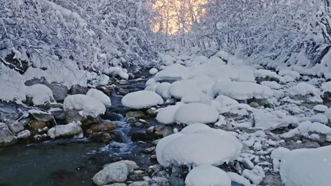 Peaceful slow motion flight over a snow-covered alpine stream with falling snow. Stock Footage 328111147