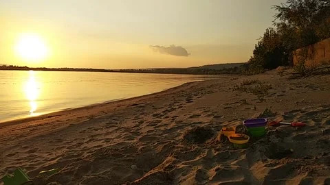Peaceful sunset scene on a sandy river beach with children’s toys Stock Footage 301777203