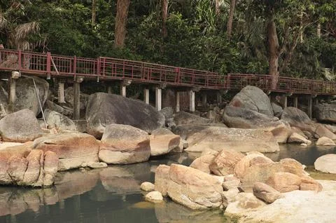 A peaceful trail with a red railing over boulders by a stream. Stock Photos