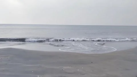 A peaceful view of the ocean waves gently washing up on a sandy beach at sunset Vidéo 334084969