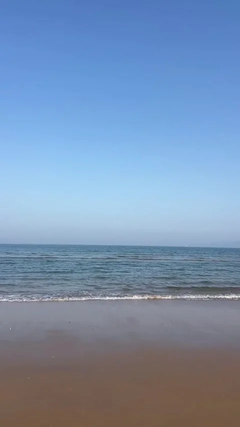 A peaceful view of the ocean waves gently rolling onto the sandy shore under a Vidéo 334163743