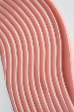 Peach-colored cosmetic texture with smooth glossy lines on a light background Stock Photos