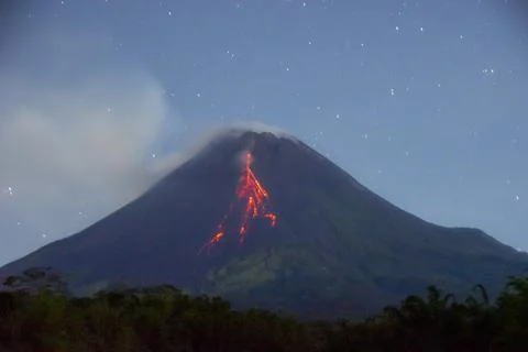 The peak of Mount Merapi spewing incandescent lava down its slopes at night Stock Photos