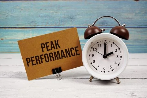 Peak Performance text written on paper card with alarm clock on wooden back.. Stock Photos
