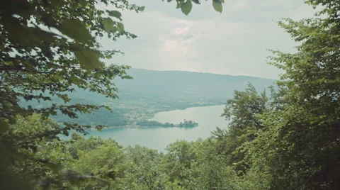 Peaking through leafs to view a big lake with mountains and a small castle Video stock 63224529