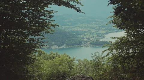 Peaking through leafs to view a big lake with mountains and a small castle Video stock 63224601