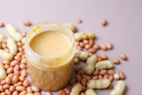 Peanut butter and raw peanuts on a colored background Stock Photos