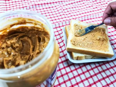 Peanut butter is being spread on bread to be served. Peanut butter is very .. Stock Photos
