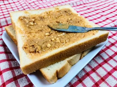 Peanut butter is being spread on bread to be served. Peanut butter is very .. Stock Photos