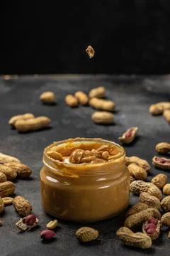 Peanut butter or paste in an open jar and peanuts in the peel scattered on .. Stock Photos