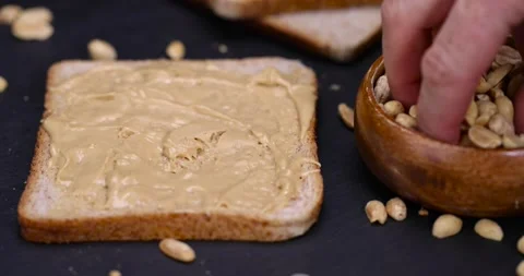 Peanut butter on a piece of bread and roasted peanuts on the table, closeup Stock Footage 304805849