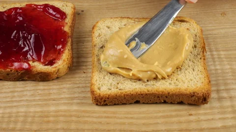 Peanut butter is spread with a knife onto a slice of multi-grain toast bread  Stock Footage 319885019
