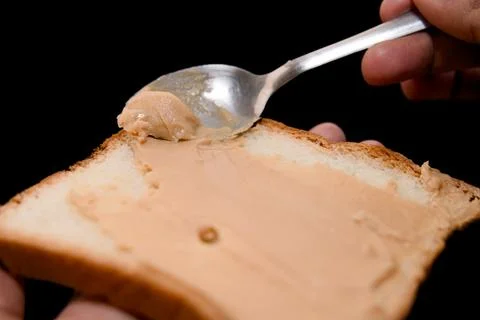Peanut butter spread on a slice of bread with a spoon Stock Photos