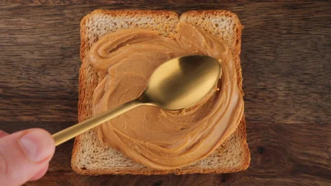 Peanut Butter Spreading on bread with a golden spoon, top view Video stock 219721341
