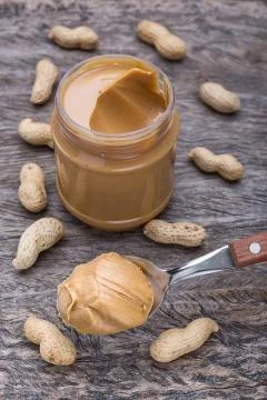 Peanut cream in spoon. On a background of nuts and container, vertical. Foto stock