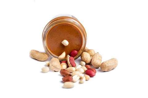 Peanut paste in a glass jar next to scattered peanuts. Isolated on a white ba Stock Photos