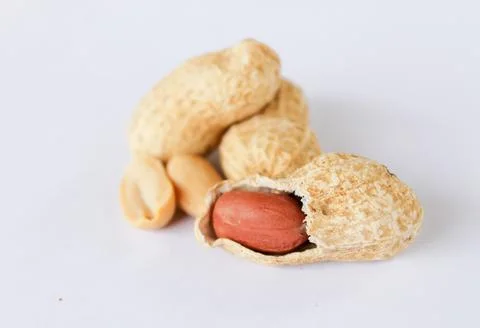 Peanuts are on a white background. One was peeled to reveal a red seed inside Stock Photos