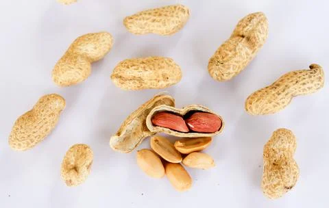 Peanuts scattered on a white background. One was opened to reveal a red seed  Foto stock