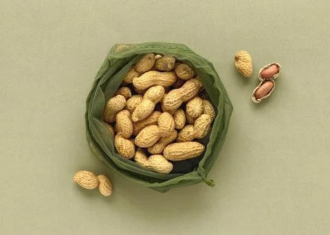Peanuts in shell and reusable mesh bag on green paper background, natural Stock Photos