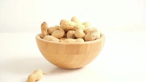 Peanuts in a shell fall into a bowl on a white background. Healthy food. Stock Footage 241479834