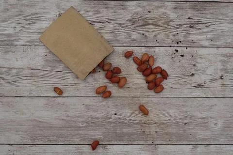 Peanuts spilling from paper bag on rustic wooden table Stock Photos