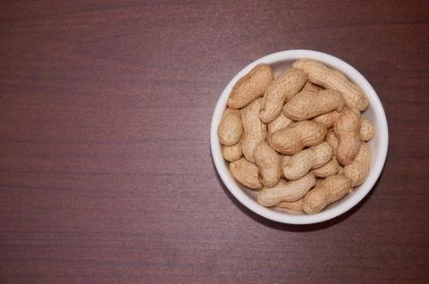 Peanuts uncleaned against a background of brown wood. Stock Photos